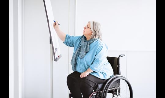 Middle-aged woman in wheelchair draws on a white board